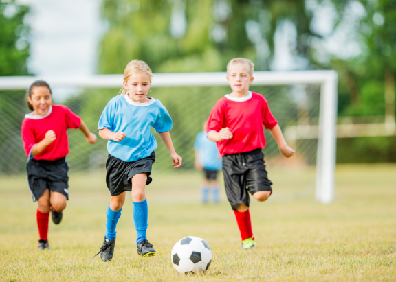 a little girl dribbles a soccer ball as two other kids on the opposite team try to catch her