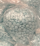 Seized M30 tablets in plastic bags. The tablets are round and come in differing shades of blue/green.