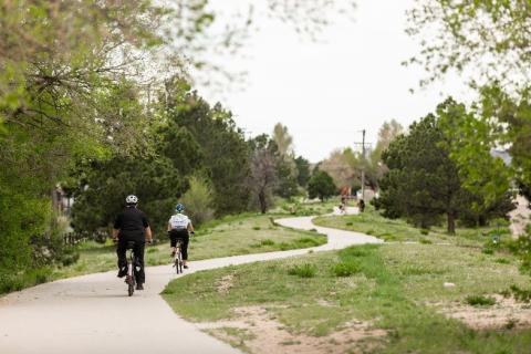 Two bikers ride their bikes down a paved urban trail.