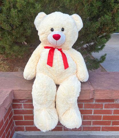 A cream-colored, giant stuffed bear with a red bow tie.