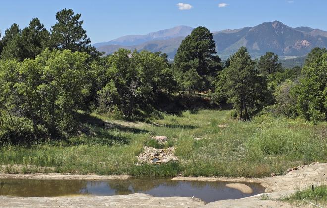 A stormwater tributary with greenery in the background, and Pikes Peak visible even further in the background.