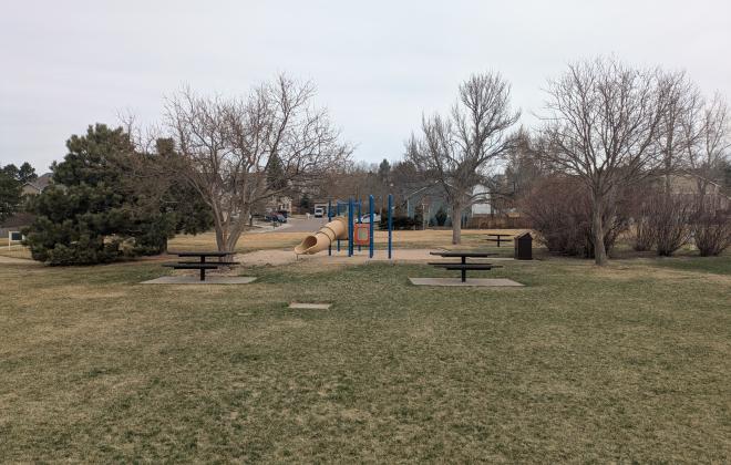 Two tables and a playground are visible at Woodland Hills Community Park on a gloomy spring day.