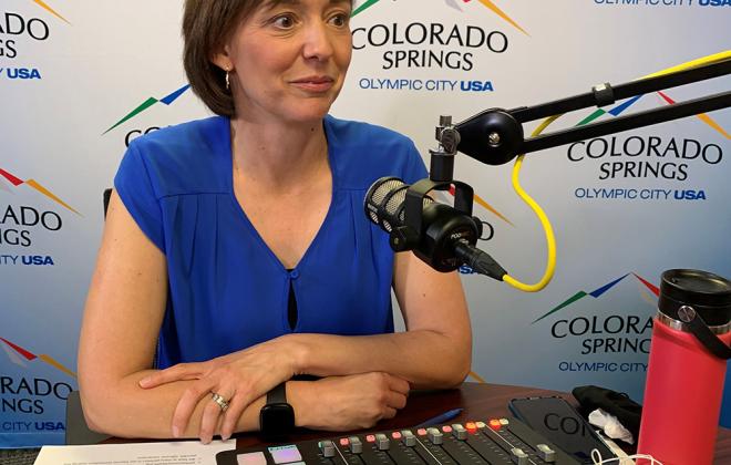 Jen sitting behind a radio microphone. A soundboard is on the table in front of her. 